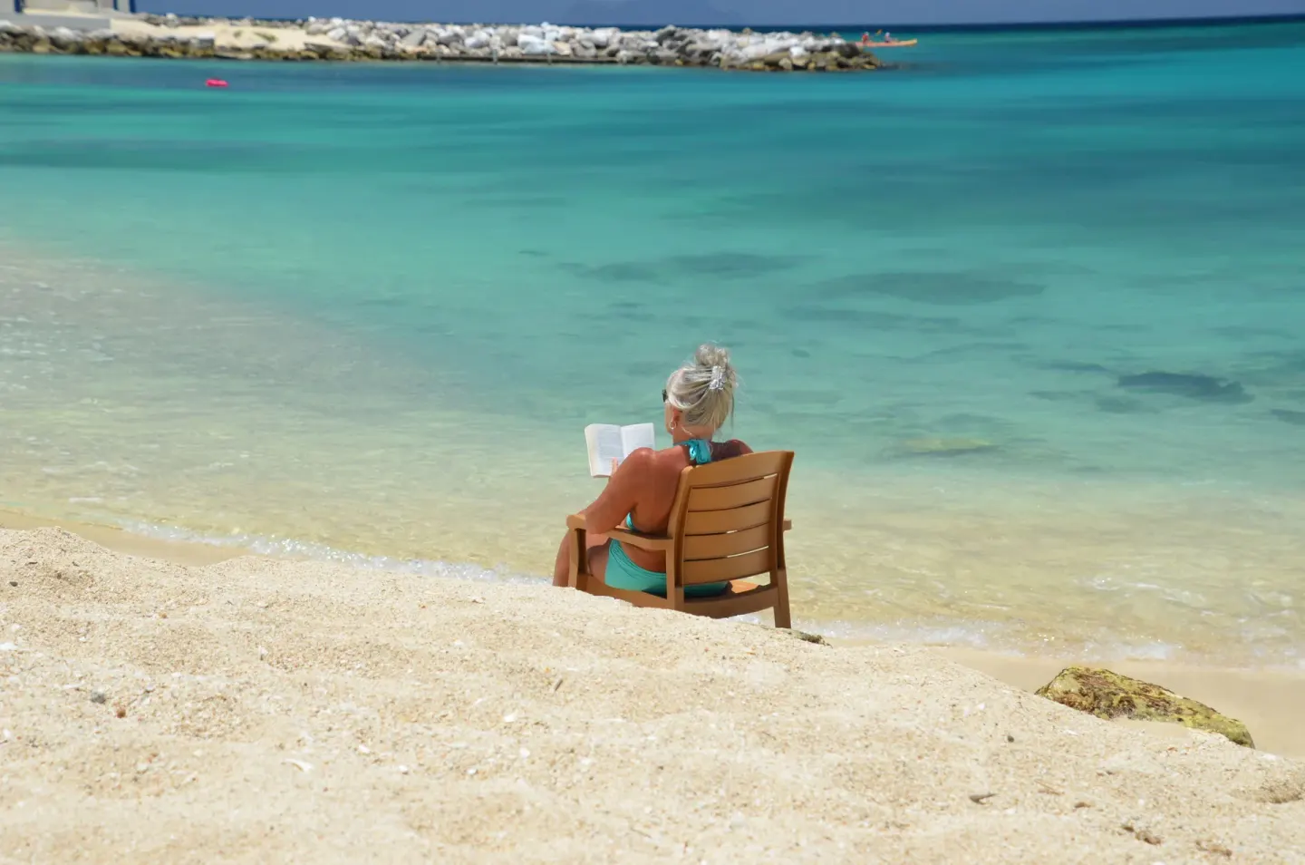 Beach chair by clear turquoise water at Simpson Bay Resort, Marina & Spa with a guest reading by the shore.