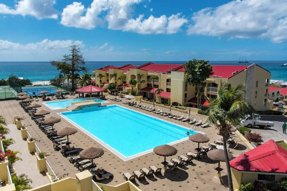 Large resort pool, lounge chairs, tennis court, and ocean backdrop at Simpson Bay Resort, Marina & Spa.