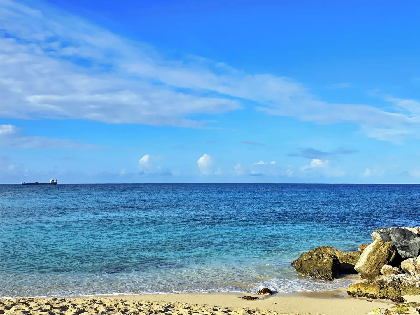 Ocean shoreline at Simpson Bay Resort, Marina & Spa with rocks, blue water, and a ship on the horizon.