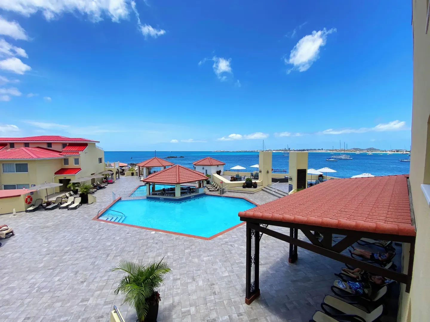 Ocean-view pool courtyard with red roofs and boats offshore at Simpson Bay Resort, Marina & Spa.