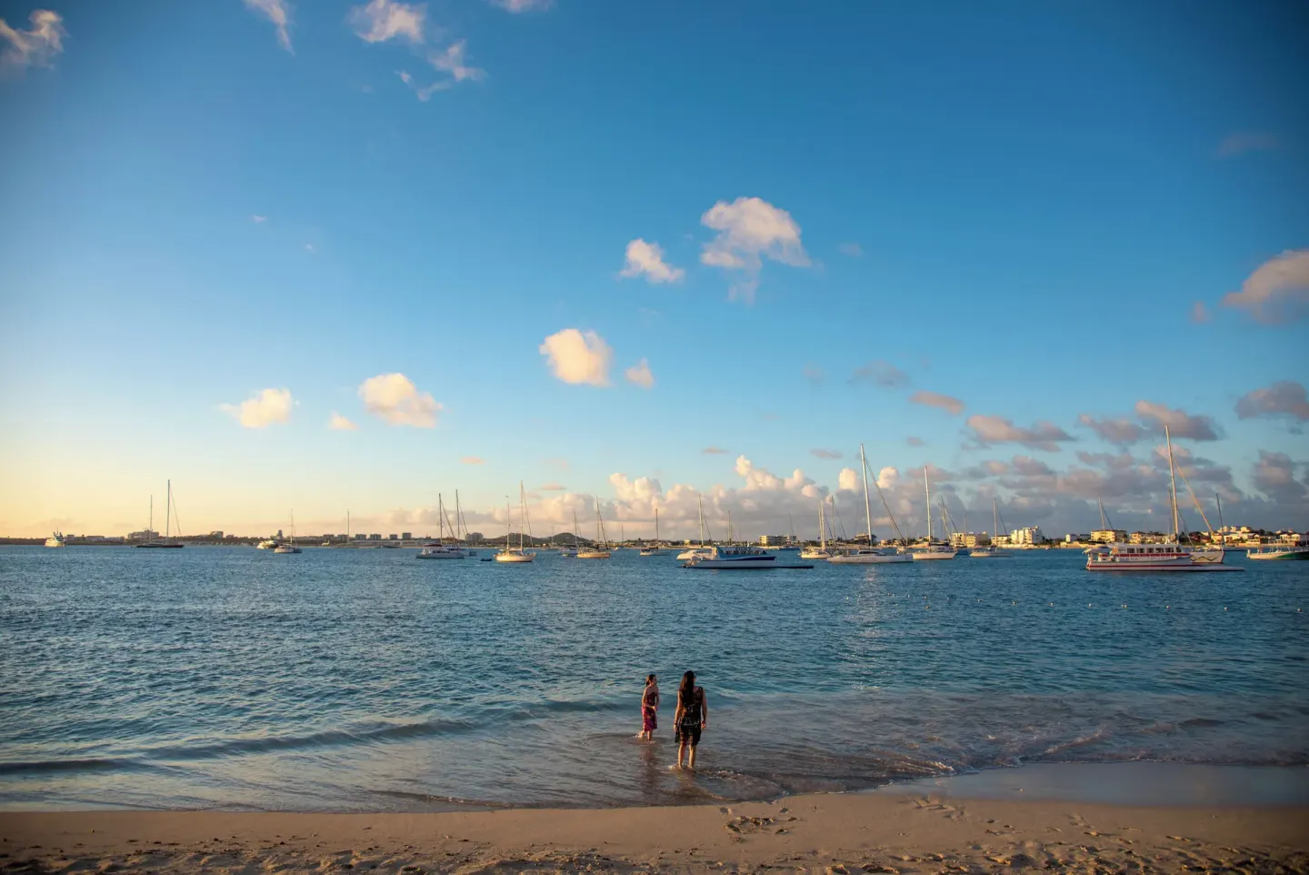 Sunset beach view at Simpson Bay Resort, Marina & Spa with people wading and boats in the bay.