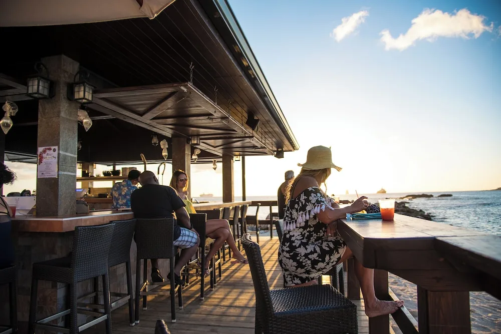 Beachside bar deck with guests by the water at Simpson Bay Resort, Marina & Spa.