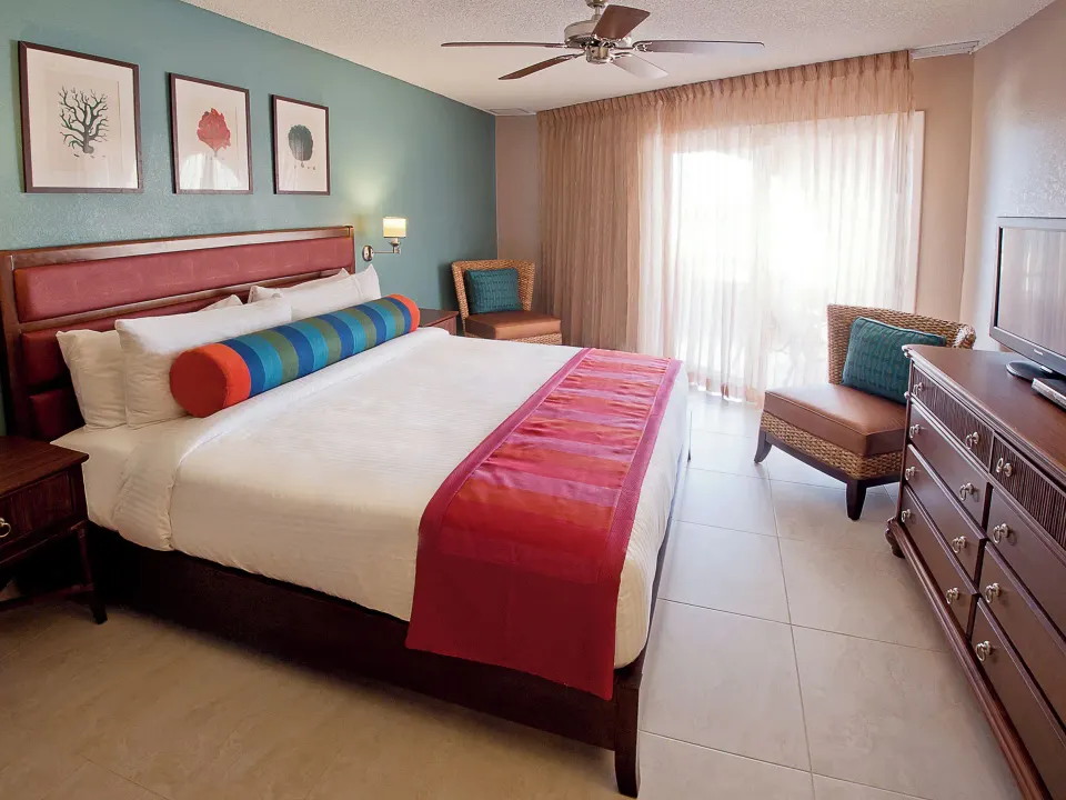 Deluxe Suite bedroom at Simpson Bay Resort, Marina & Spa with king bed, dresser, TV, and balcony curtains.