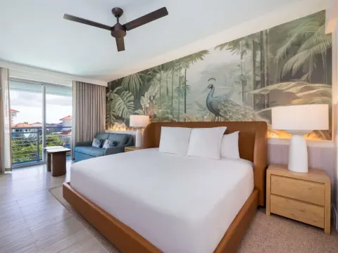 King bed guest room with balcony, blue sofa, and tropical mural at SLS Baha Mar.