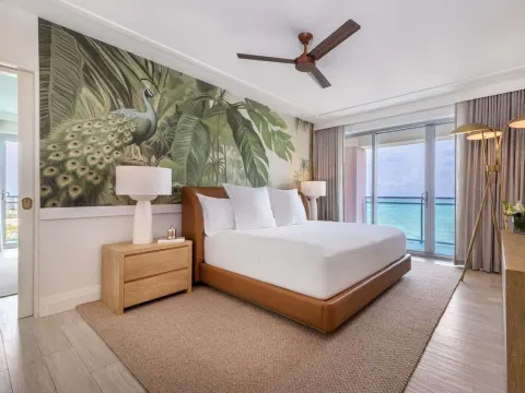 King bed guest room with ocean-facing balcony and peacock mural at SLS Baha Mar.