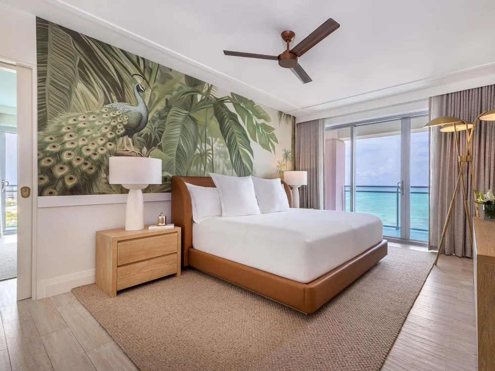 King bed guest room with ocean-facing balcony and peacock mural at SLS Baha Mar.