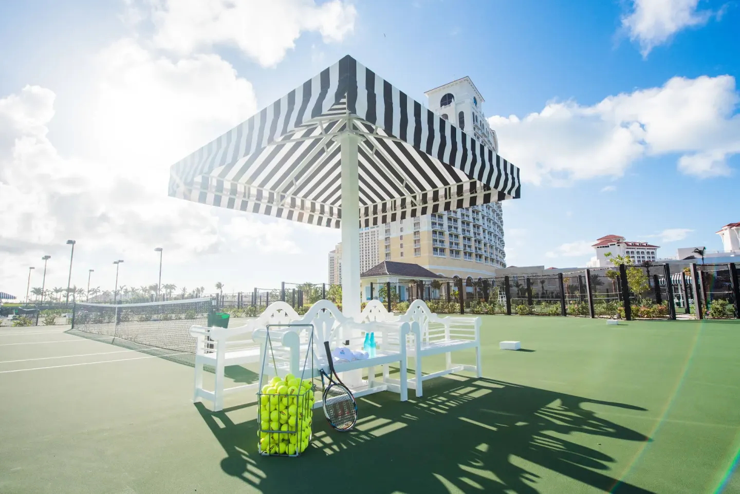 Tennis court with striped shade canopy and rackets at SLS Baha Mar.