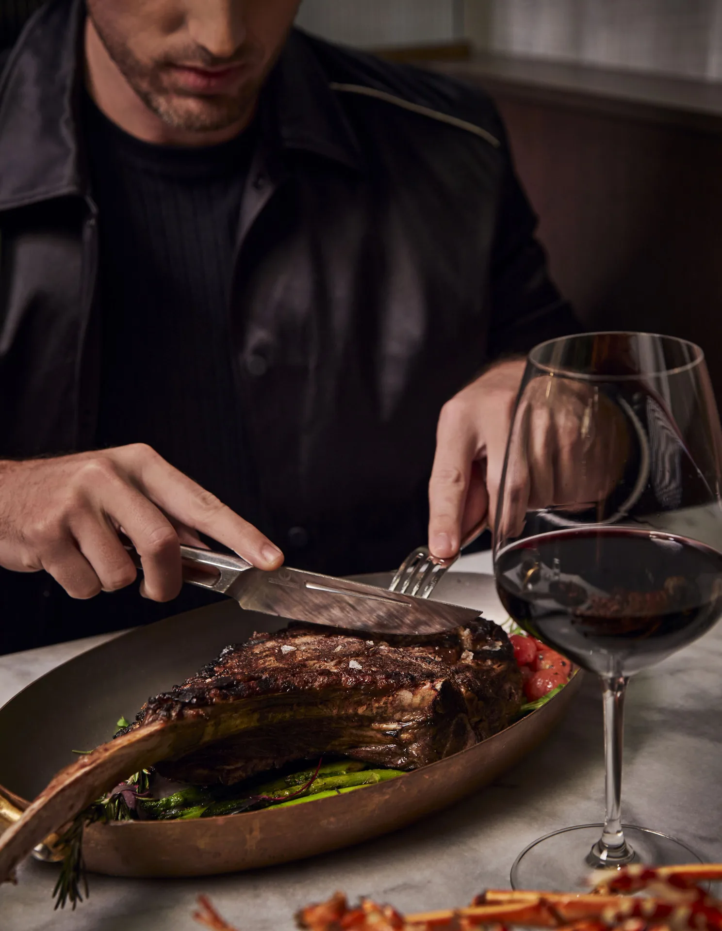 Diner slicing a bone-in steak beside a glass of red wine at SLS Baha Mar.