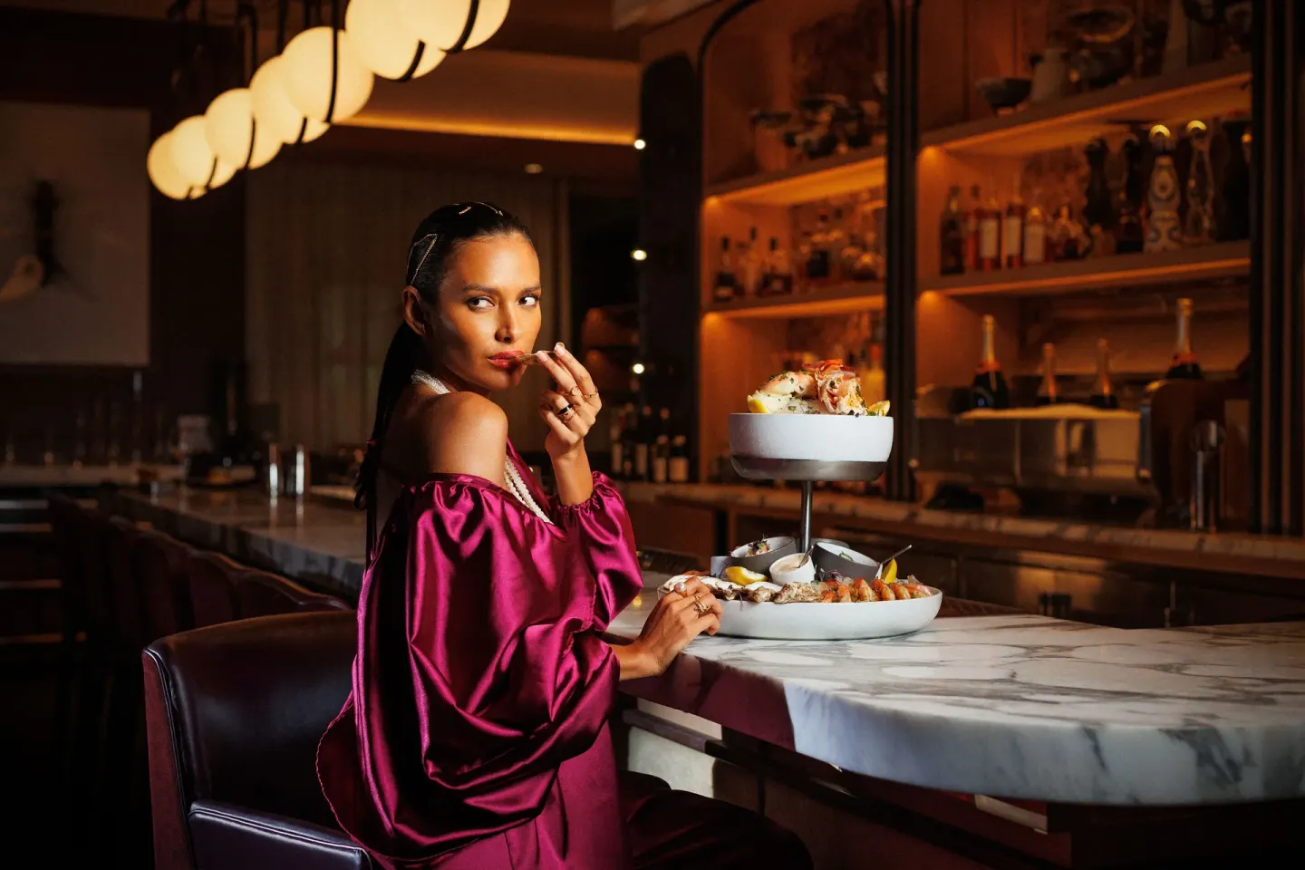Guest seated at a marble bar with a tiered seafood platter at SLS Baha Mar.