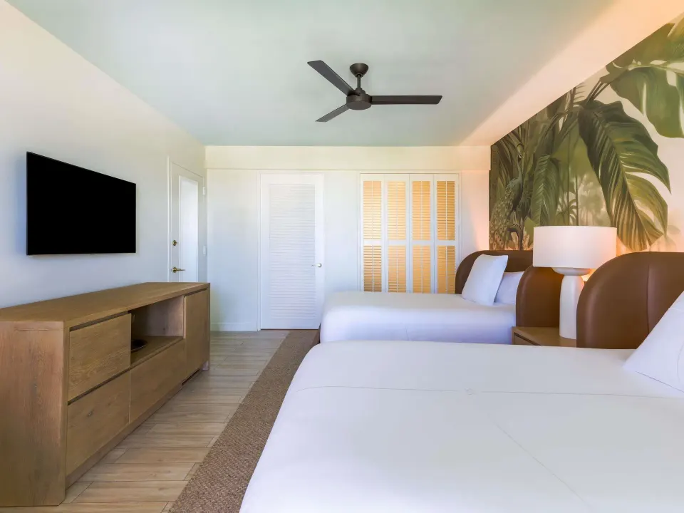 Superior Queens room with two beds, wall TV, wood console, and tropical mural at SLS Baha Mar.