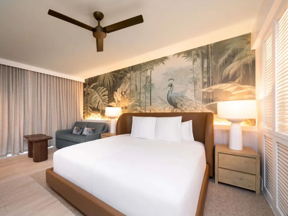 Superior king room with tropical mural, sofa, and bedside lamps at SLS Baha Mar.