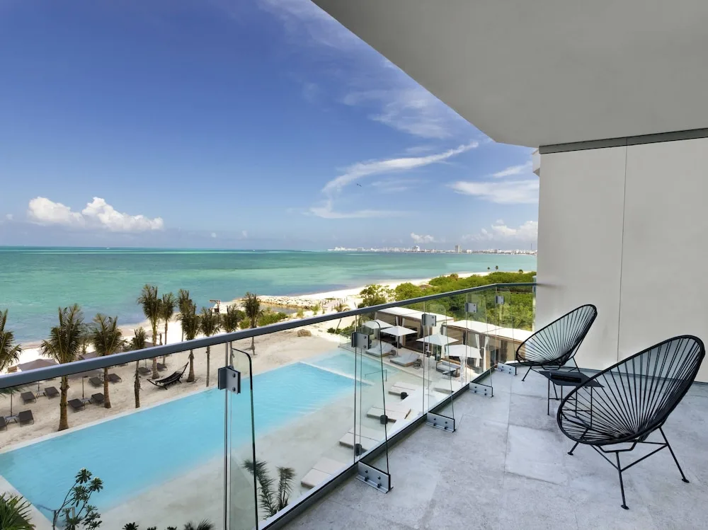 Balcony with black chairs overlooking the pool, beach, and turquoise sea at SLS Cancun.