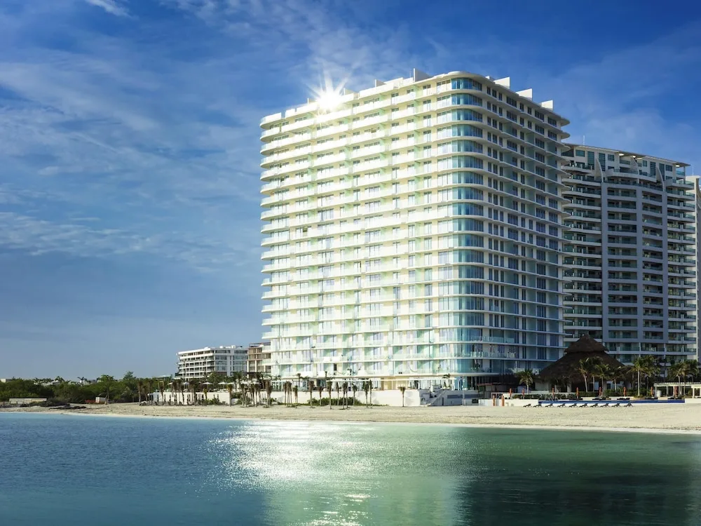 Beachfront exterior of SLS Cancun with the tower reflected in calm water.