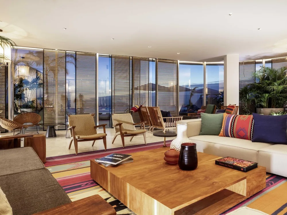 Colorful lobby lounge with sofas, wood chairs, plants, and large windows at SLS Cancun.