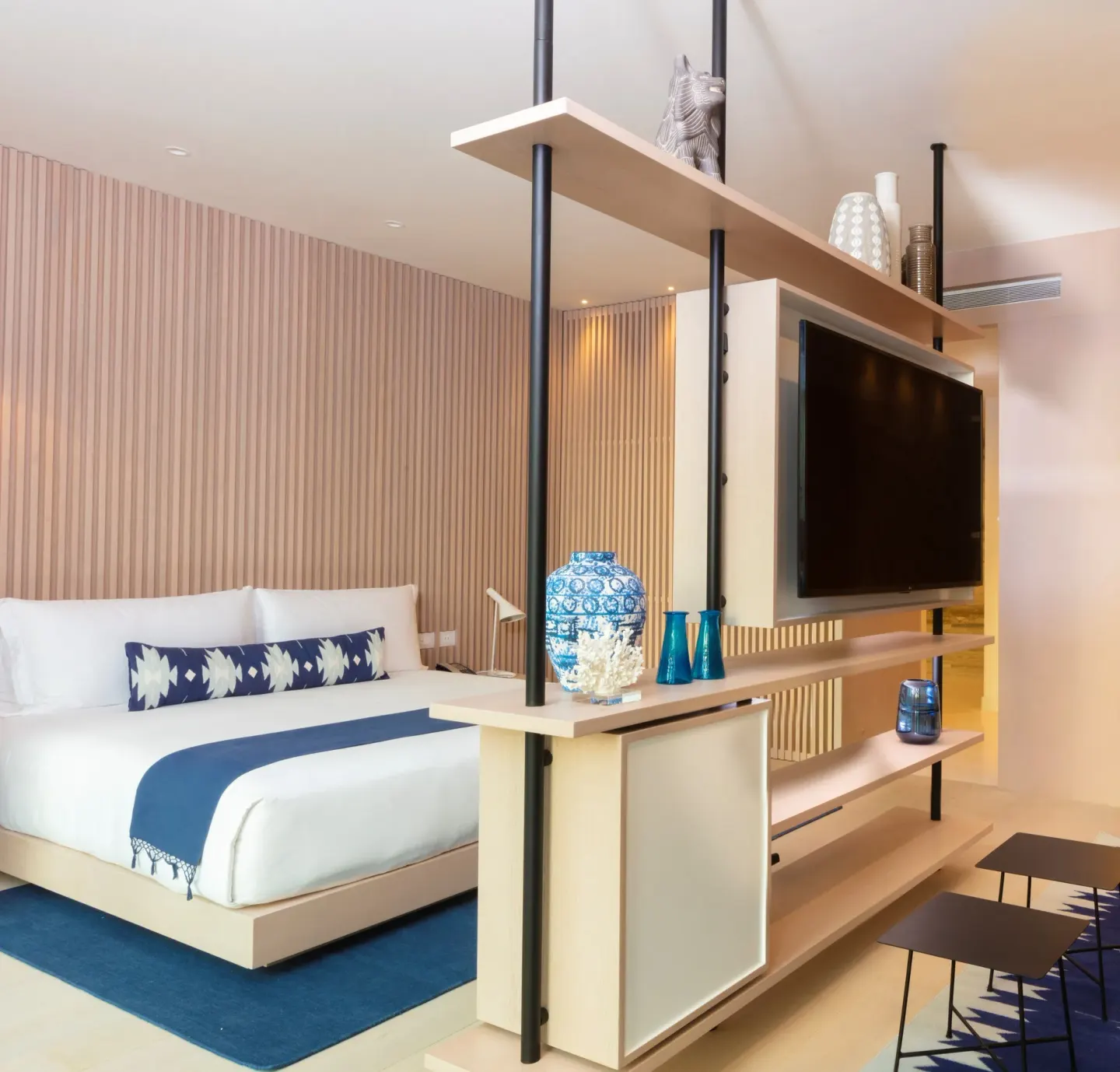 Guest room with a king bed, TV divider, blue accents, and open shelving at SLS Cancun.