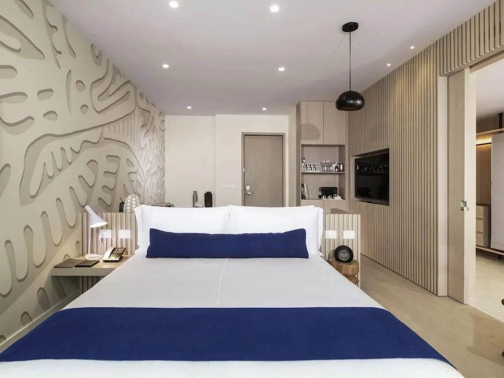 King bed guest room with patterned wall, minibar shelving, and open closet at SLS Cancun.