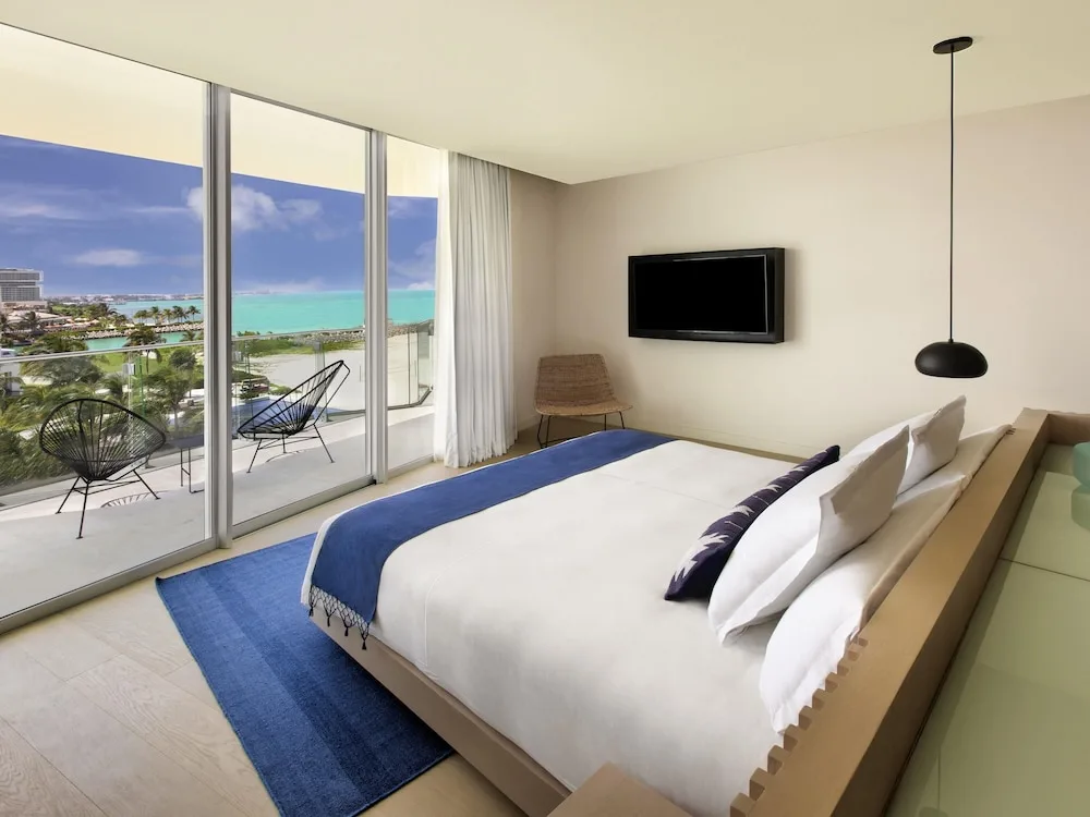 King bed guest room with balcony chairs and turquoise water view at SLS Cancun.