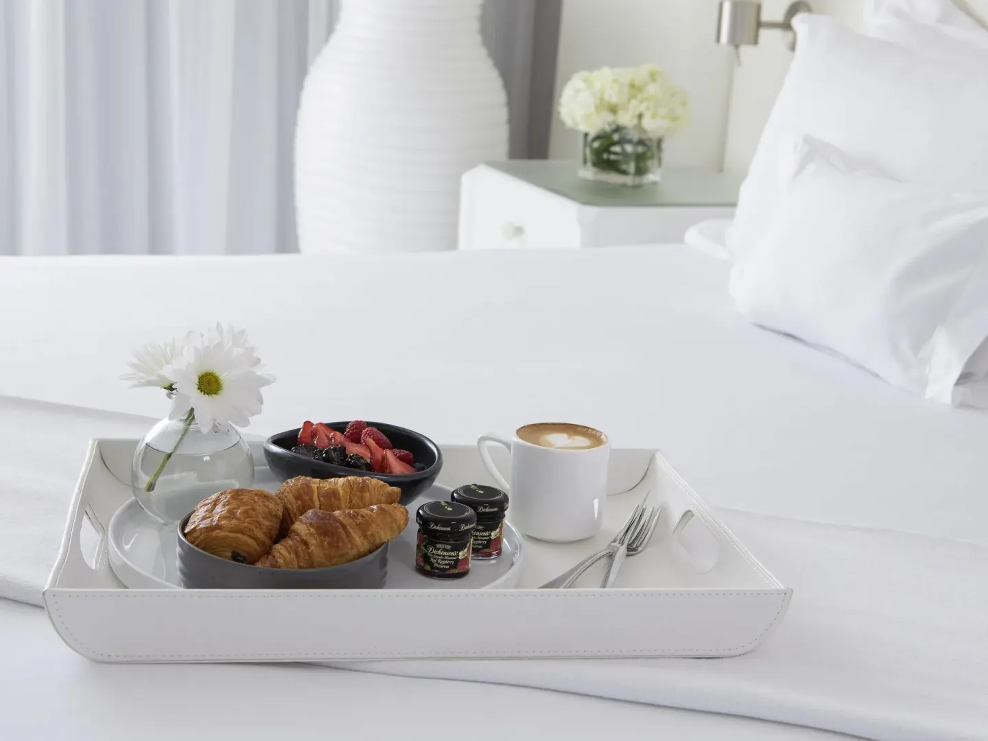 Breakfast tray with pastries, fruit, coffee, and flowers on a white bed at SLS Cancun.