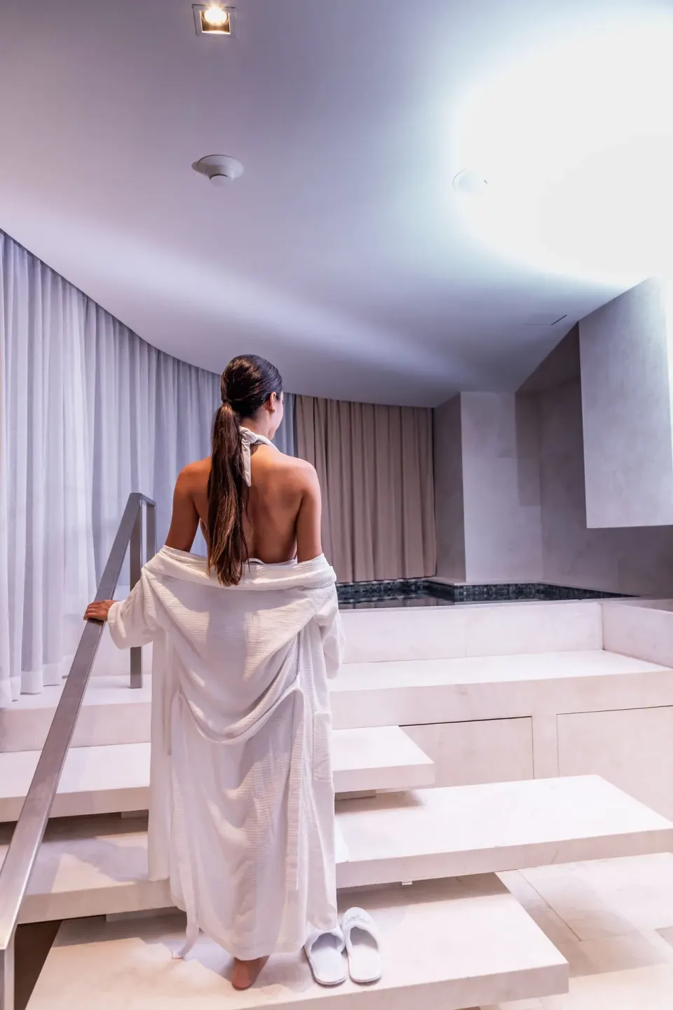 A guest in a white robe steps toward an indoor spa pool at SLS Cancun.