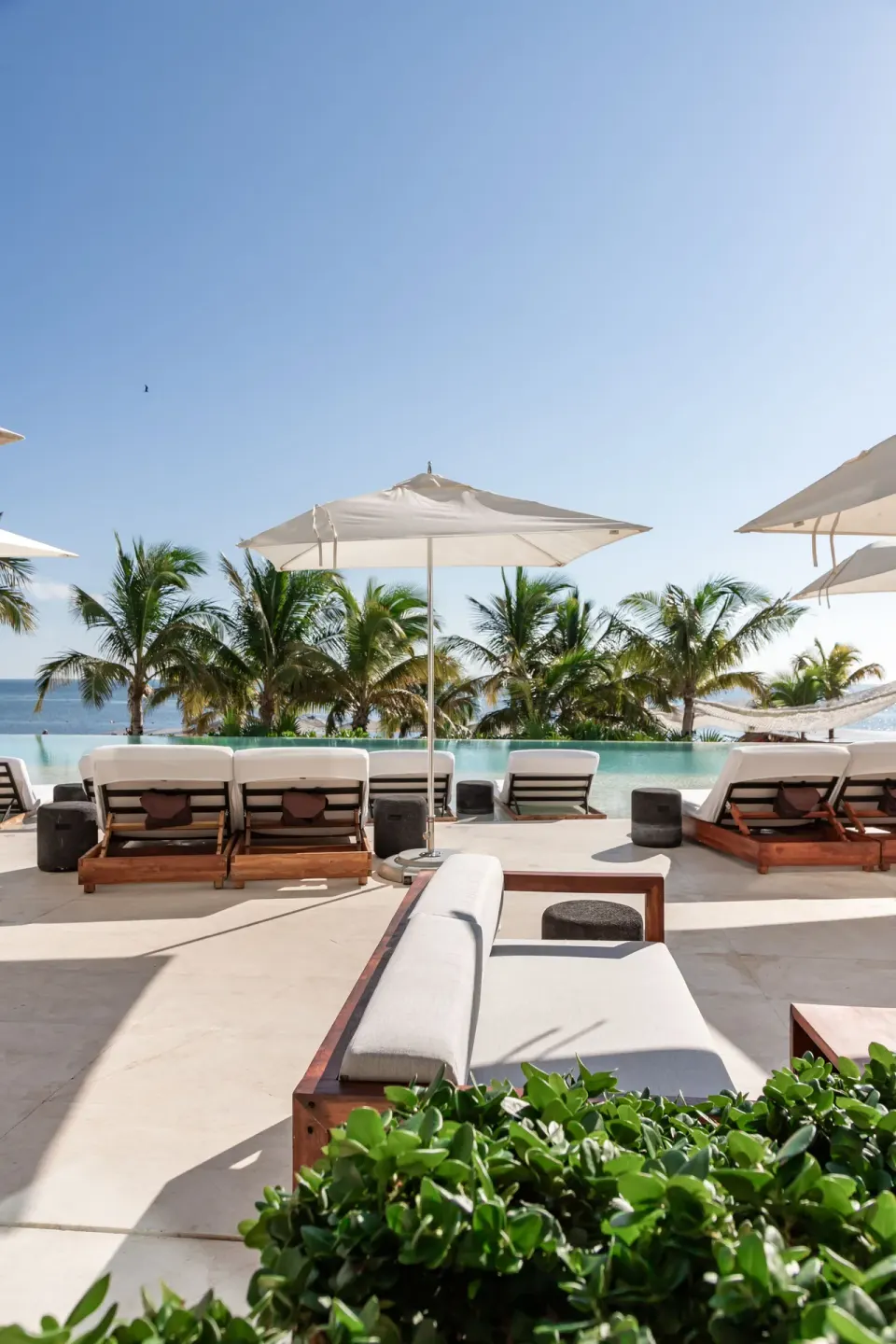 Pool deck with loungers, umbrellas, palms, and ocean beyond at SLS Cancun.
