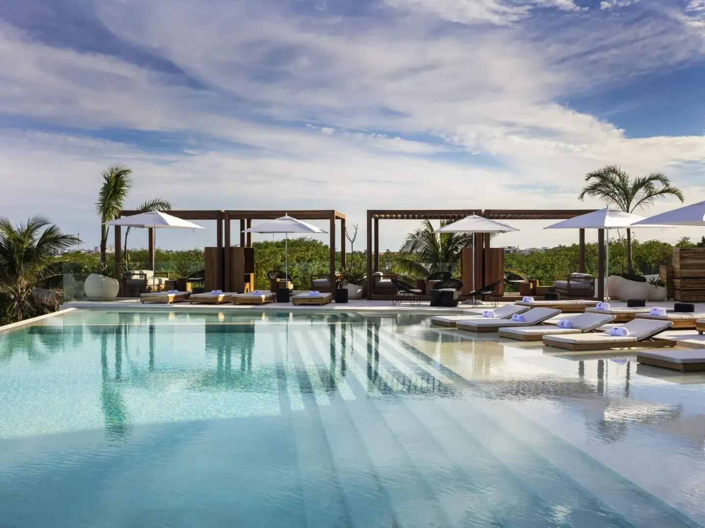 Pool terrace at SLS Cancun with loungers, umbrellas, cabanas, and palms.