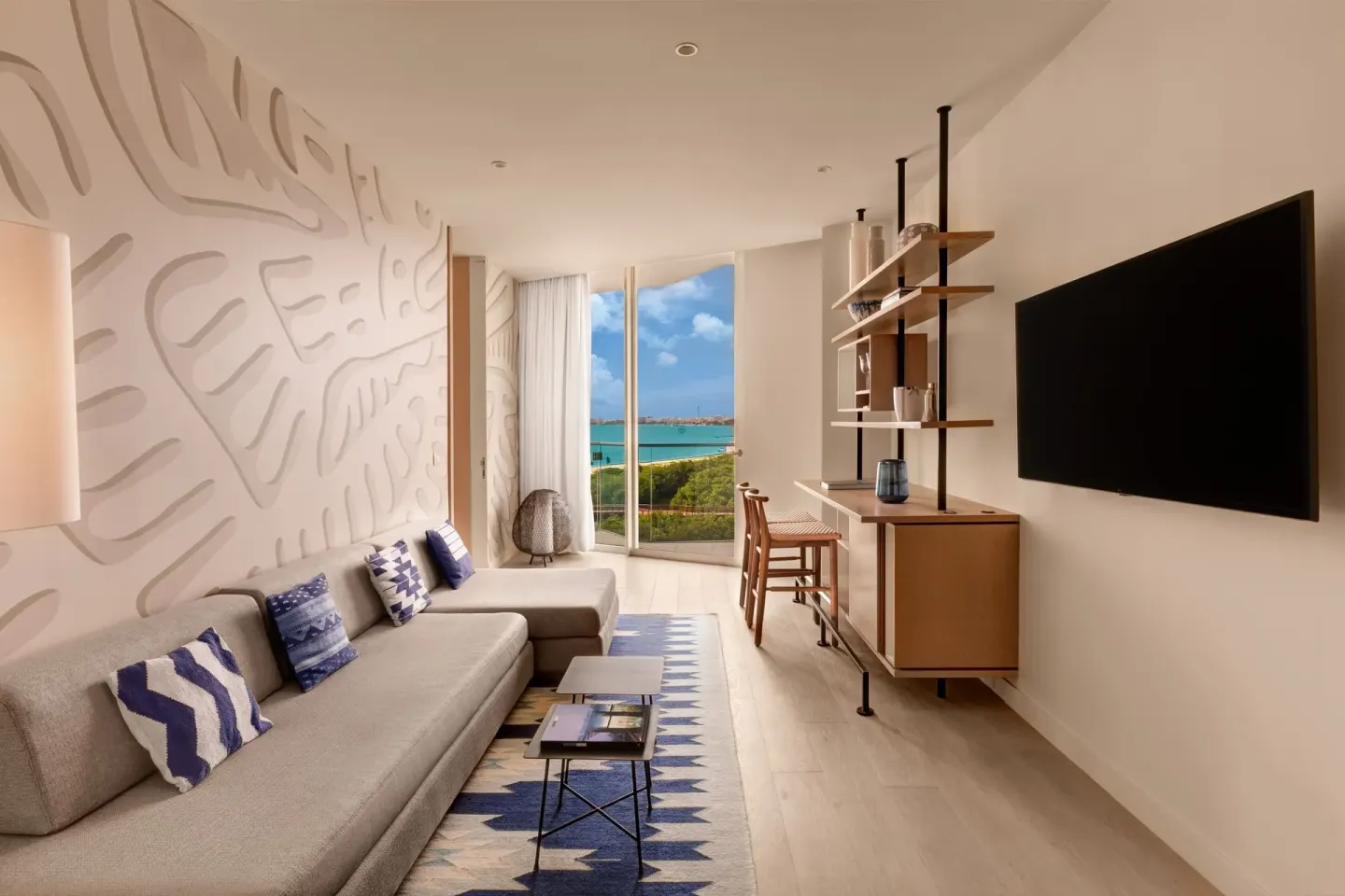 Narrow suite living room with sofa, wall TV, desk, and water view at SLS Cancun.
