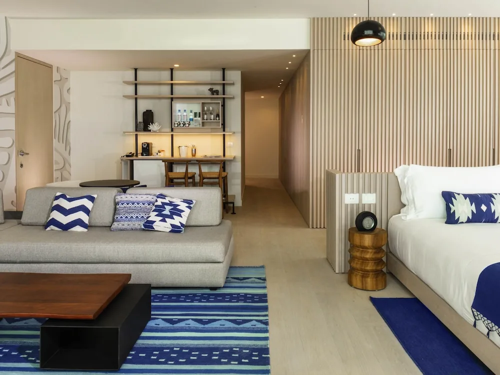 Suite seating area with sofa, king bed, striped rug, and bar shelving at SLS Cancun.
