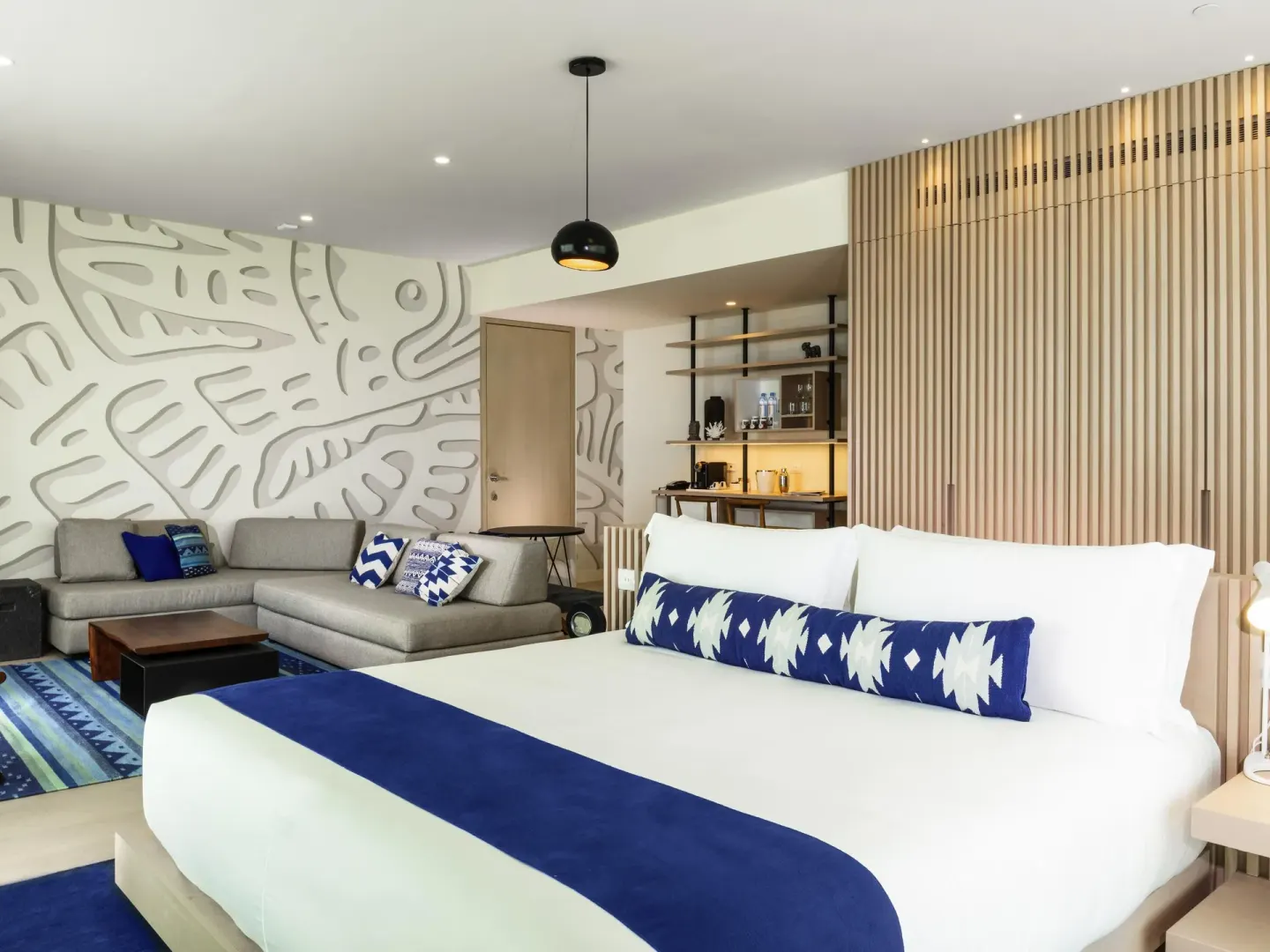 Suite with king bed, sofa, blue rug, and minibar shelving at SLS Cancun.