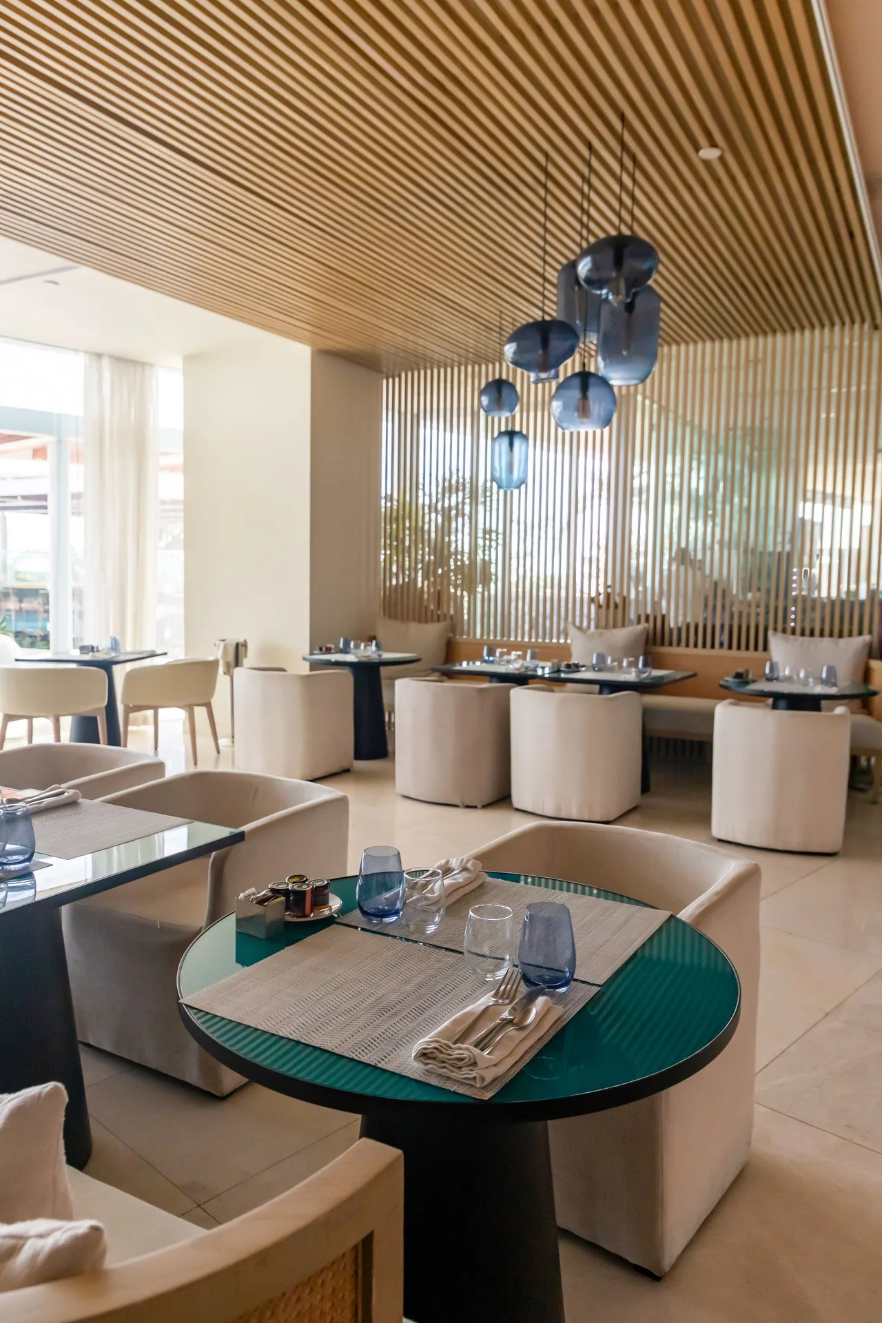 Modern dining room with round tables, cream chairs, and wood slat ceiling at SLS Cancun.