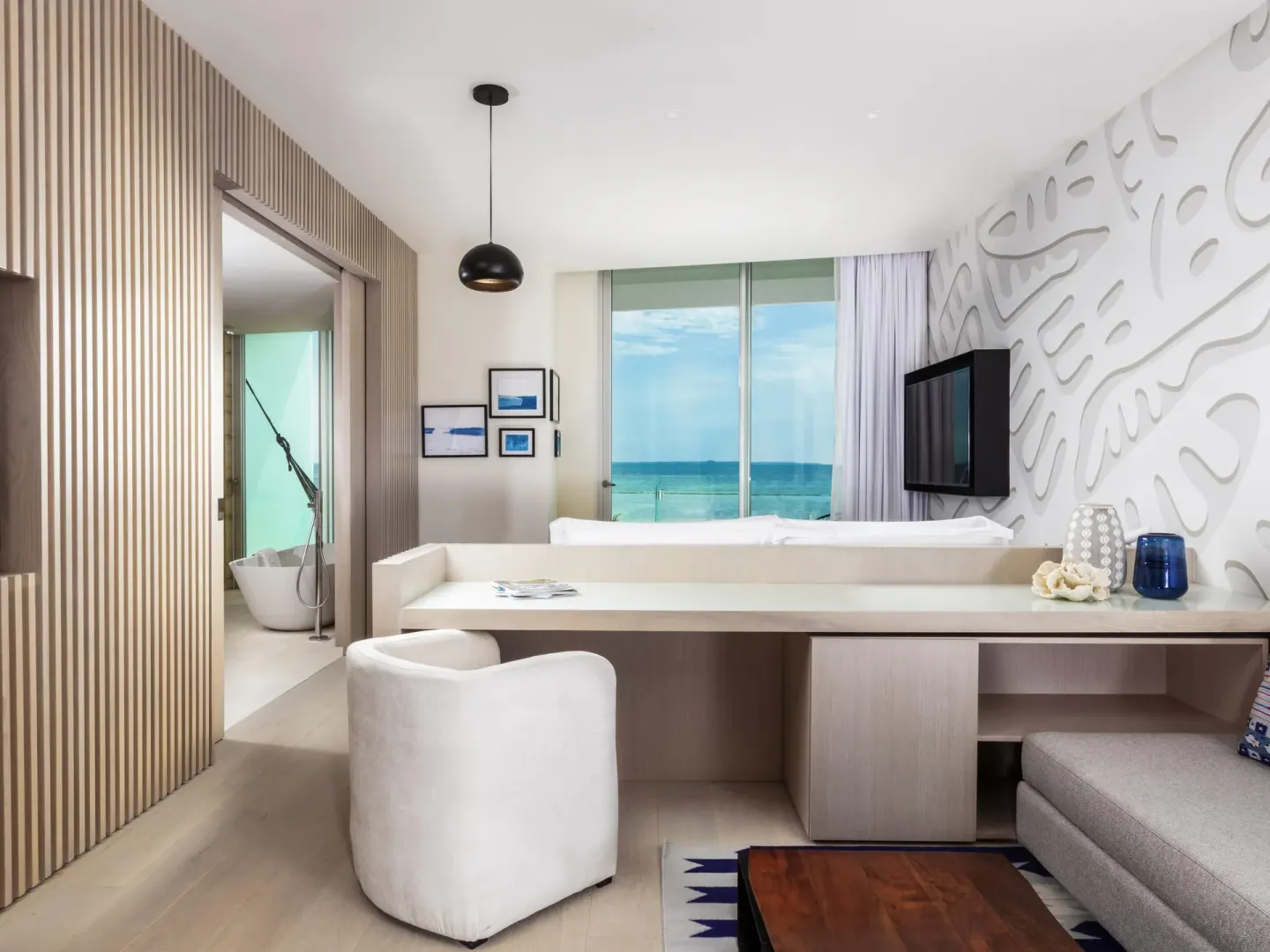 Deluxe Room Oceanfront at SLS Cancun with desk, sofa, TV and ocean view beyond the bed.