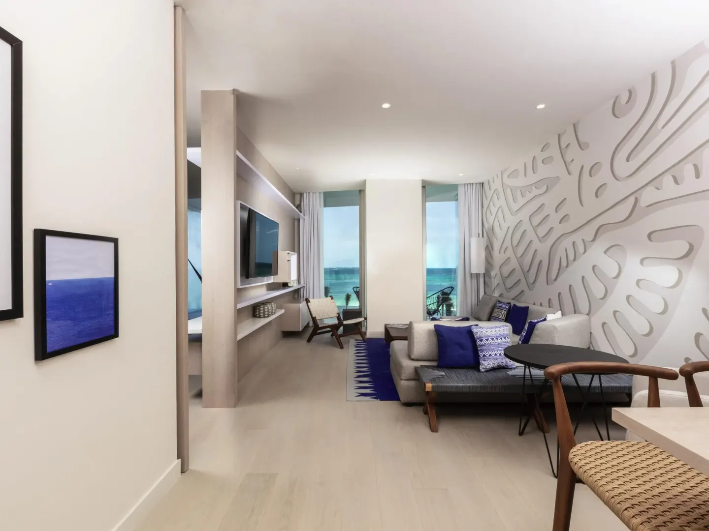 Deluxe oceanfront suite living room with sofa, TV and tall windows at SLS Cancun.