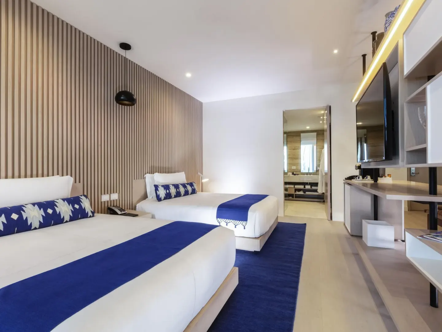Deluxe oceanfront suite bedroom with two beds and media shelving at SLS Cancun.