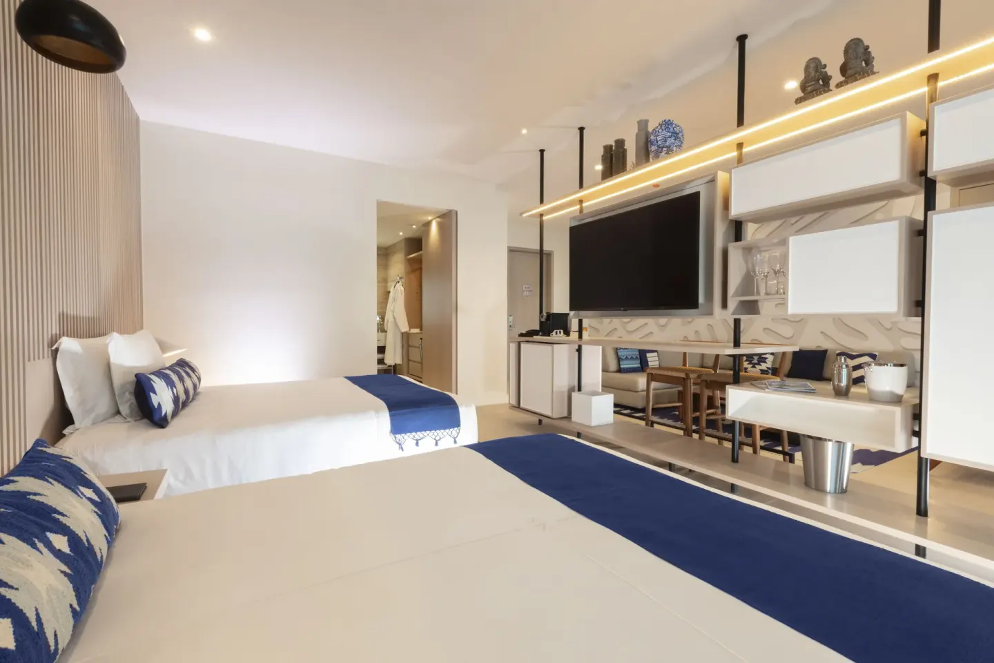 Deluxe oceanfront suite bedroom with two beds, TV wall and open shelving at SLS Cancun.