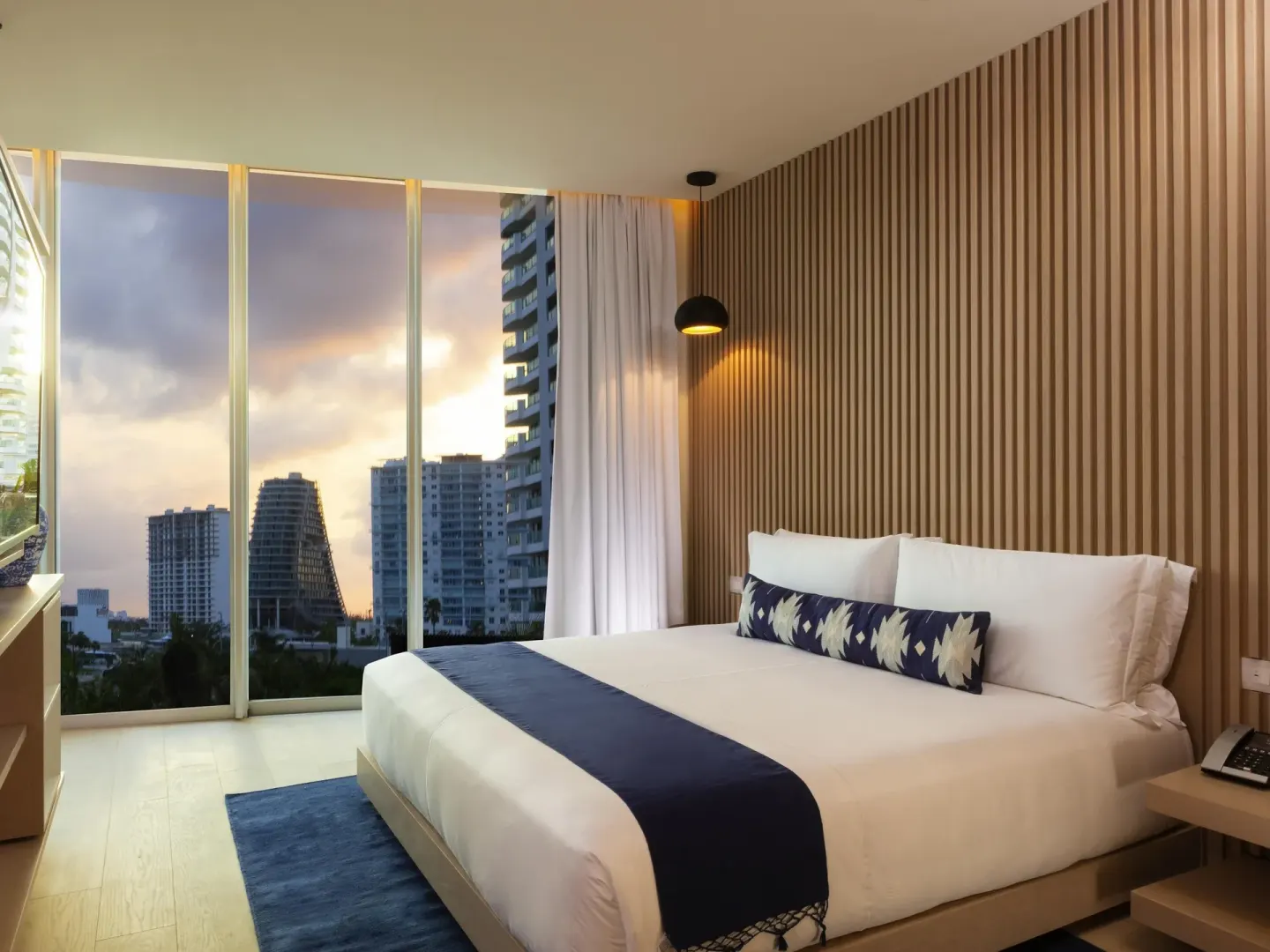 Superior Room king bed beside floor-to-ceiling windows with city buildings outside at SLS Cancun.