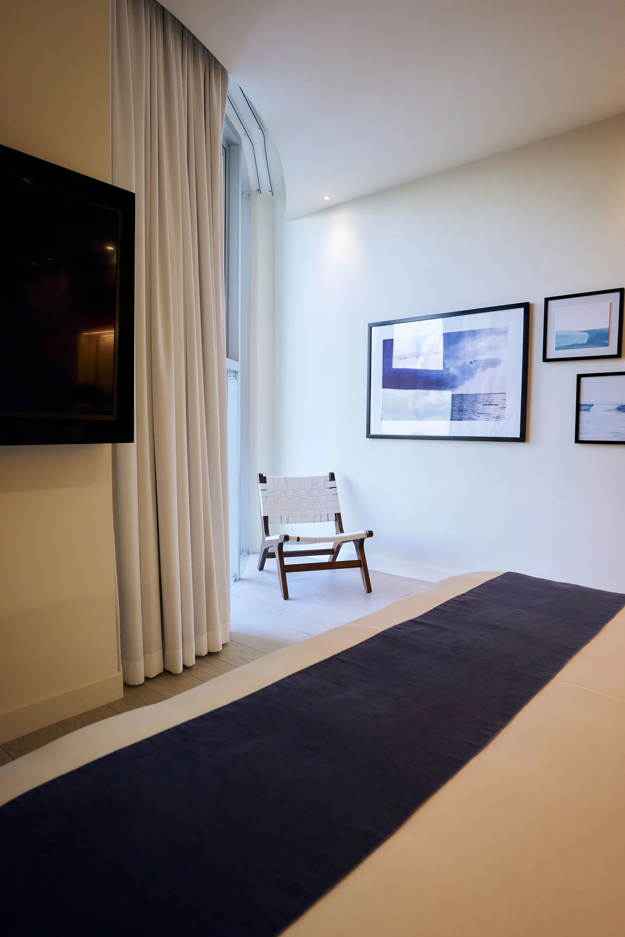 Superior Room bed corner with wall-mounted TV, chair, curtains, and framed art at SLS Cancun.