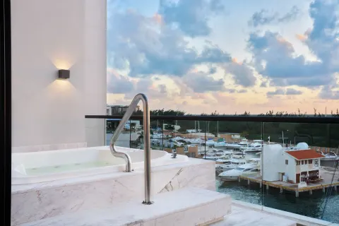 Balcony soaking tub overlooking a marina at sunset at SLS Playa Mujeres.