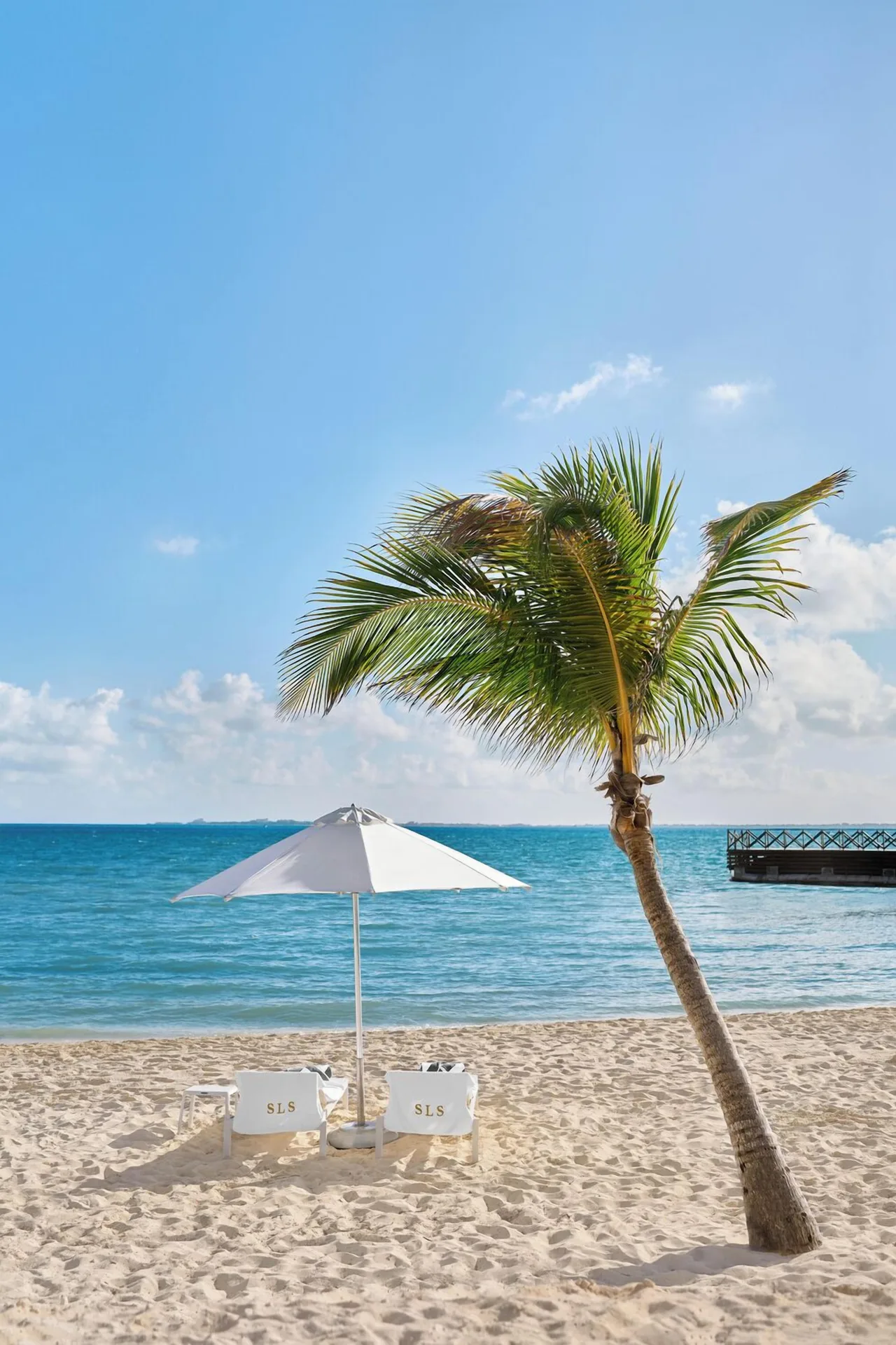 Beach loungers and umbrella face the turquoise sea at SLS Playa Mujeres.