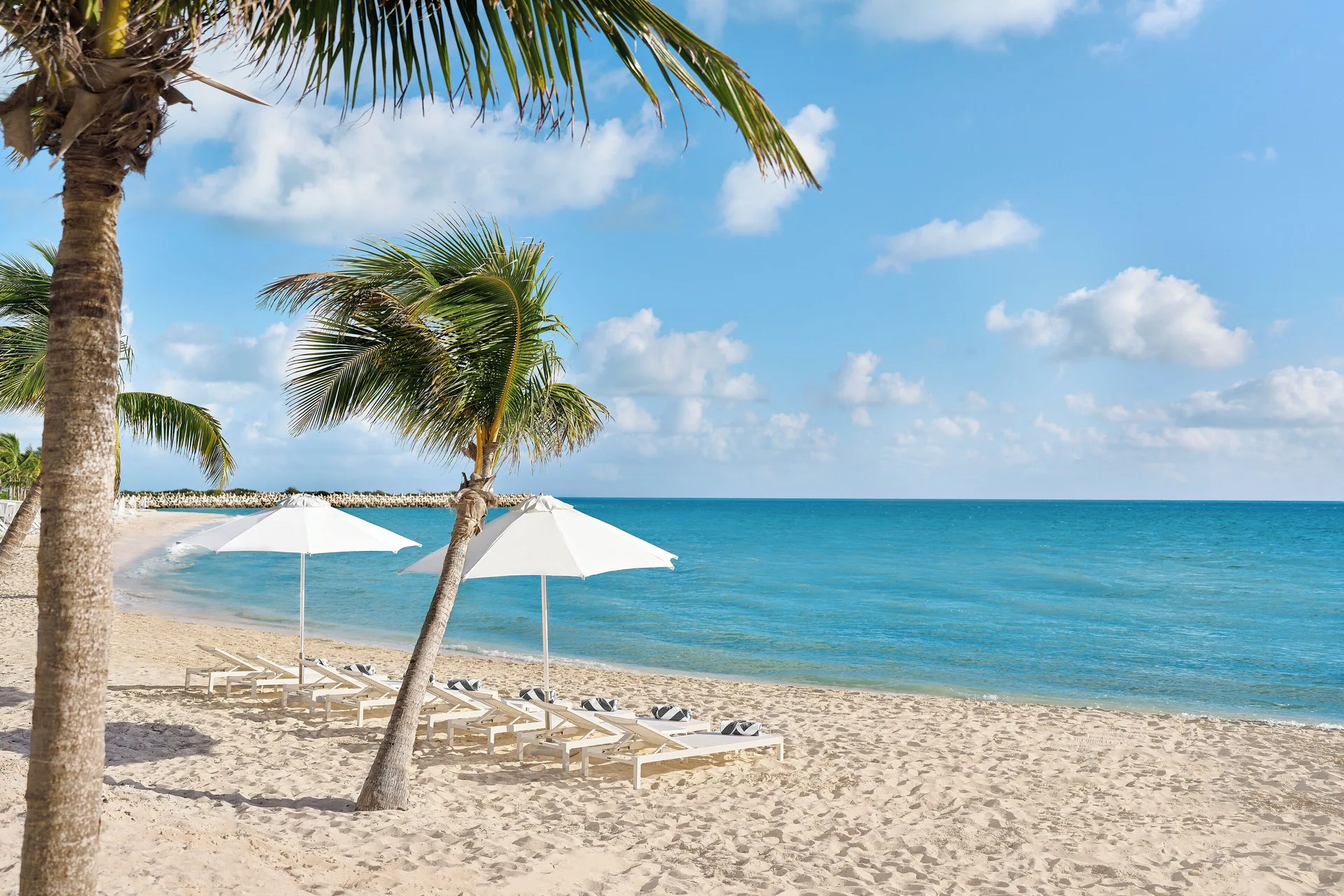 Beach loungers and white umbrellas by turquoise water at SLS Playa Mujeres.