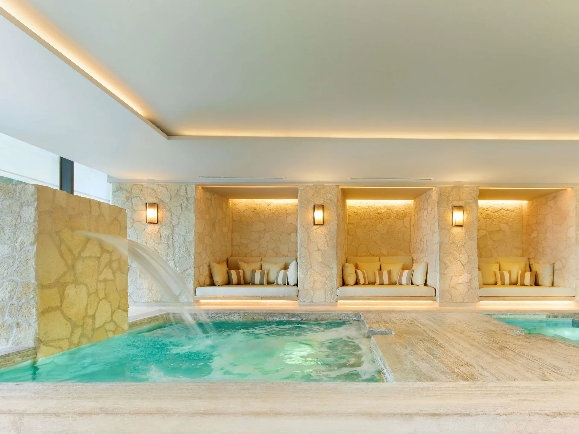 Indoor spa pool with a water feature and cushioned alcoves at SLS Playa Mujeres.