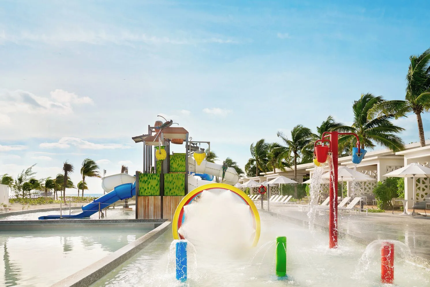 Splash pad with slides, spray features, and palm trees at SLS Playa Mujeres.