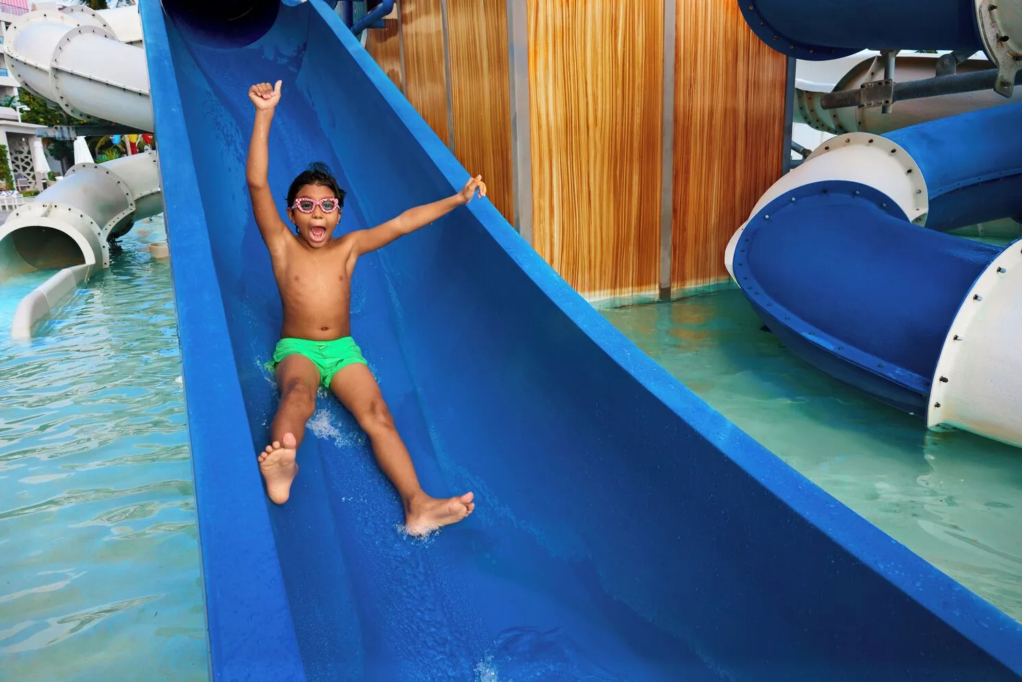 Child sliding down a blue water slide at the splash area of SLS Playa Mujeres.