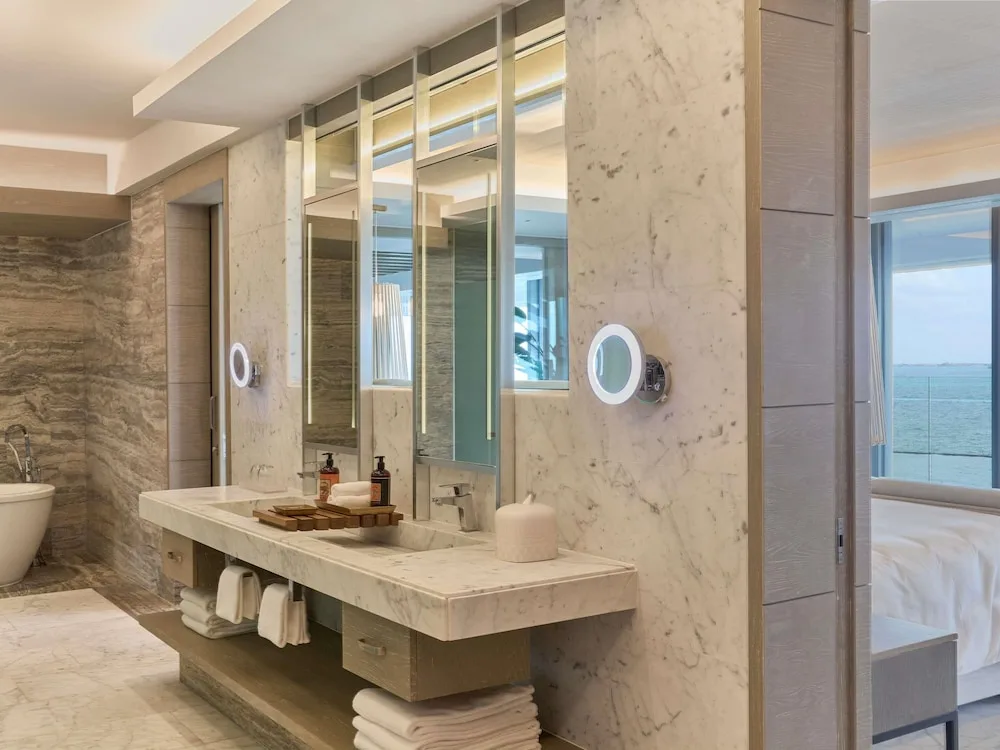 Marble bathroom vanity with lit mirrors beside a guest room at SLS Playa Mujeres.