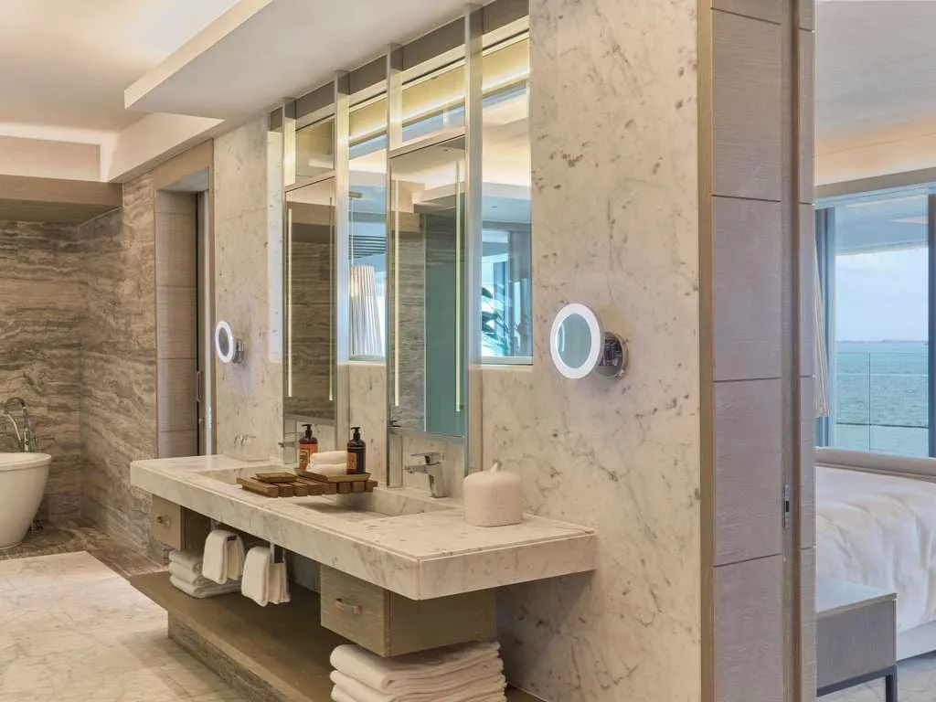 Guest room bathroom with marble vanity and ocean glimpse at SLS Playa Mujeres.