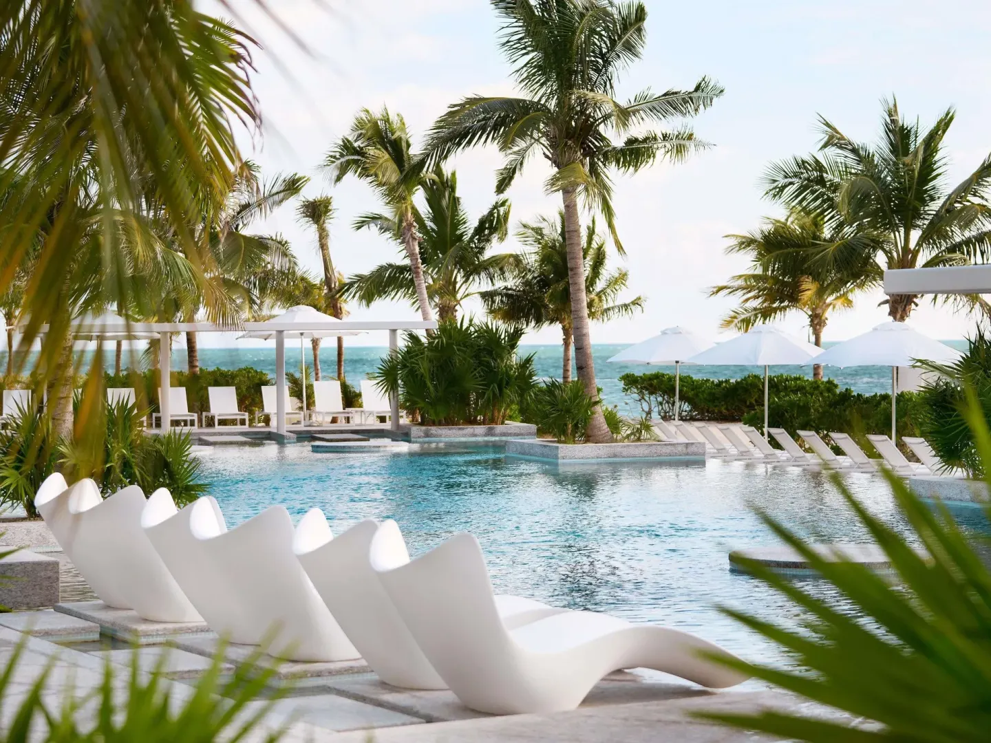 Palm-framed pool with white loungers and ocean beyond at SLS Playa Mujeres.