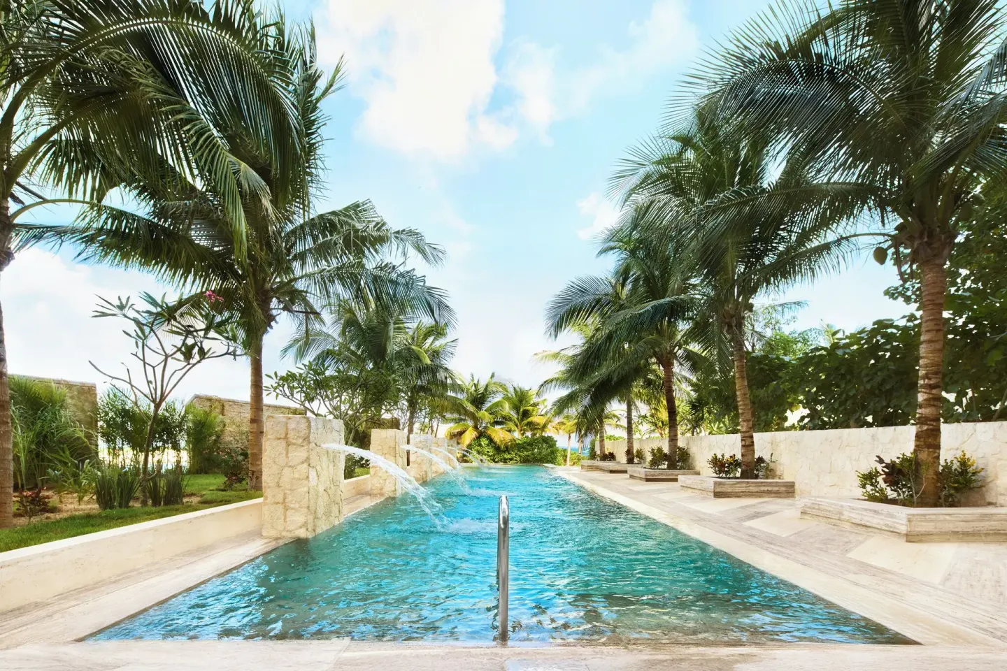 Palm-lined outdoor pool with stone walls and water spouts at SLS Playa Mujeres.