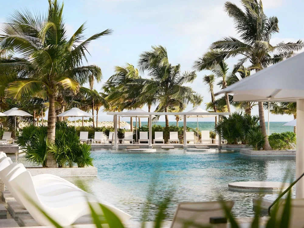 Quiet pool with palms, cabanas and white loungers at SLS Playa Mujeres.
