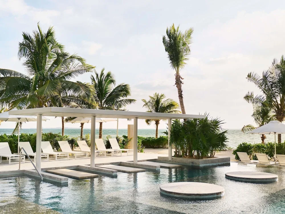 Pool platforms, white loungers and ocean-facing palms at SLS Playa Mujeres.
