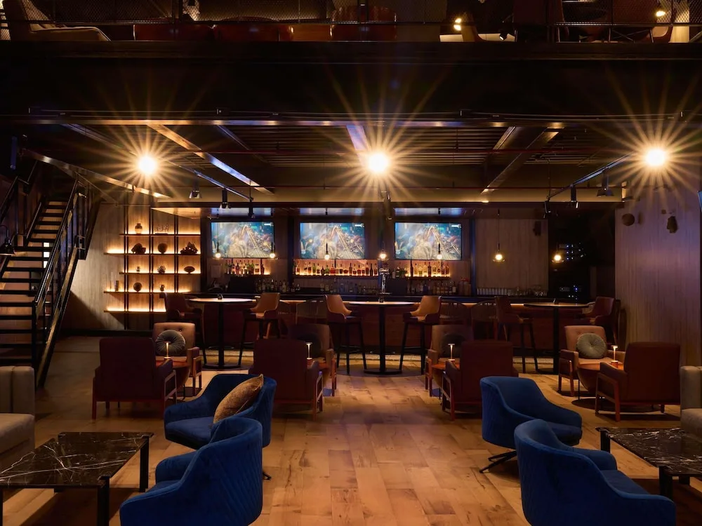 A dim lounge bar with blue chairs, warm lights, and a back bar at SLS Playa Mujeres.