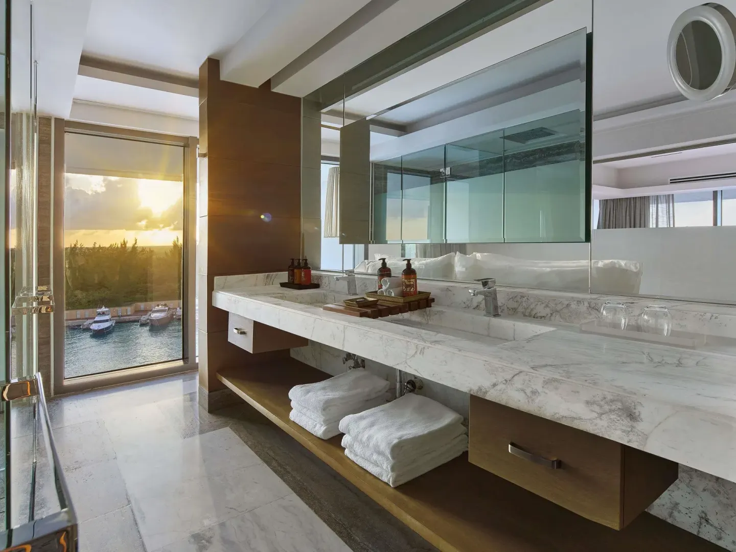 Marble bathroom vanity with towels, glass shower, and sunset window in a suite at SLS Playa Mujeres.