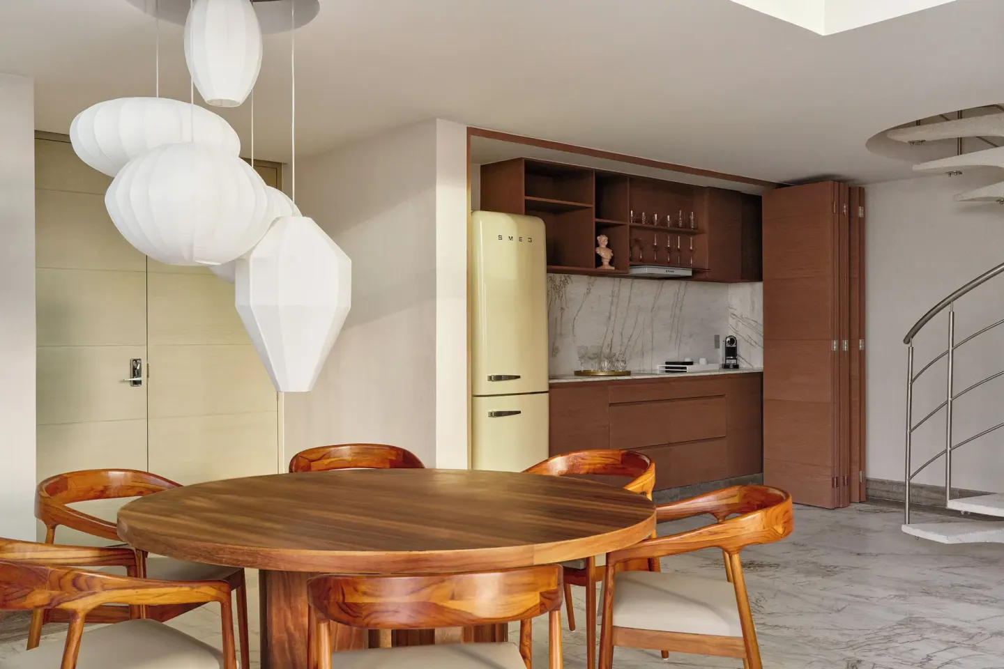 Round dining table, kitchenette, pendant lights, and spiral stair in a suite at SLS Playa Mujeres.